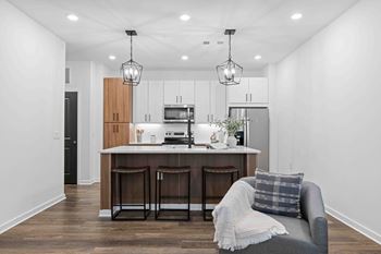 A modern kitchen with a bar stool and a grey sofa.